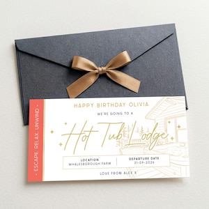 May include: A charcoal grey envelope with a gold ribbon bow and a rectangular gift voucher. The white card features gold text reading HAPPY BIRTHDAY OLIVIA, WE'RE GOING TO A Hot Tub Lodge, LOCATION WHALESBOROUGH FARM, DEPARTURE DATE 31-09-2026, LOVE FROM ALEX X.