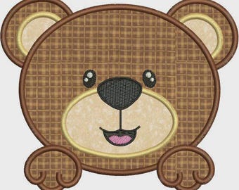 May include: Embroidered bear face with a waffle-like pattern in shades of brown. The bear has a black nose, small black eyes, and a pink mouth. The design includes a light tan face and ears, outlined in brown.