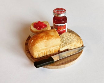 May include: A miniature wooden cutting board with a loaf of bread, a slice of bread, a small jar of Smucker's strawberry preserves, and a miniature knife.
