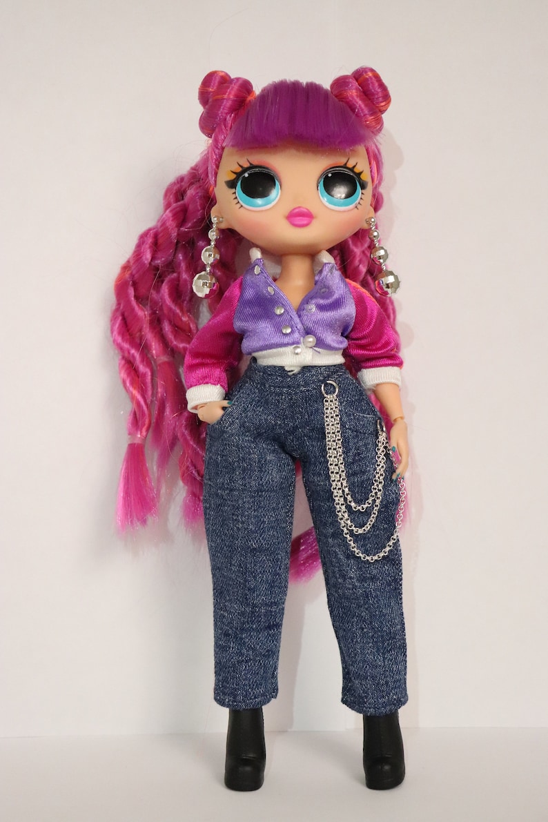 May include: A pink and purple fashion doll with long pink hair, wearing a purple and pink jacket, blue jeans, and black boots. The doll has large blue eyes and pink lips.