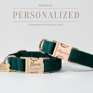 May include: Two personalized dog collars in a dark green velvet fabric with gold metal hardware. The collars are engraved with the names "Nova" and "Popcorn". The smaller collar has a matching engraved dog tag with the name "Nova" and a phone number.