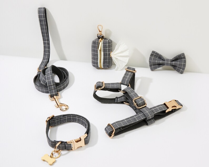 May include: A set of dog accessories in a gray and white plaid pattern. The set includes a leash, collar, harness, and bow tie. The accessories are all made of a soft, durable fabric and feature gold-tone hardware.