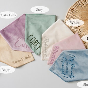 Puede incluir: Un surtido de pa&ntilde;uelos personalizados en varios colores, incluyendo rosa empolvado, verde salvia, beige, blanco, rosa y azul. Cada pa&ntilde;uelo presenta texto bordado, con nombres y frases como "My Parents Are Getting Married!"