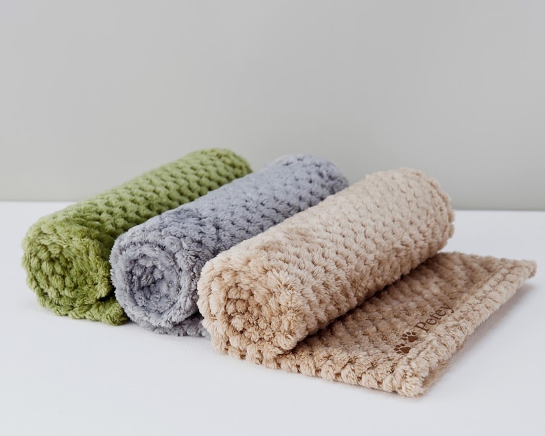May include: Three rolled-up pet blankets in green, gray, and beige. The beige blanket is unrolled and has the word "Petey" embroidered on it.