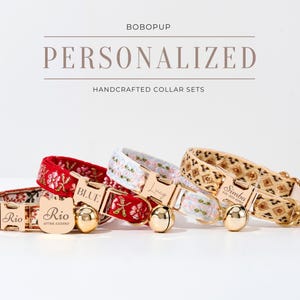 May include: Three personalized cat collars with gold buckles and bells. The collars are red with floral embroidery, white with floral embroidery, and beige with a geometric pattern. The collars are labeled "Rio", "Blue", and "Simba".