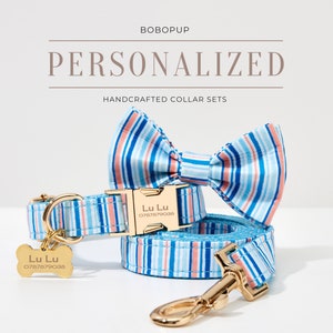 May include: A personalized dog collar set with a matching bow tie and leash. The set features a blue and white striped pattern with gold-colored hardware. The collar and tag are engraved with the name "Lu Lu" and a phone number.