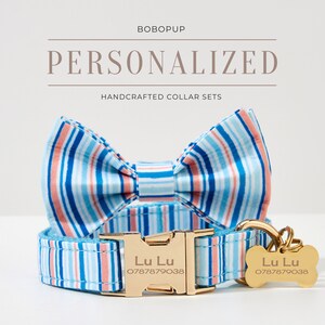 May include: Personalized dog collar set with a striped pattern in blue, coral, and white. The set includes a collar, bow tie, and a bone-shaped tag with the name "Lu Lu" and a phone number. The collar has a gold-colored buckle.