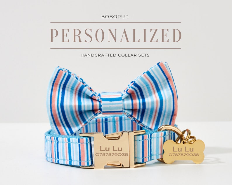 May include: Personalized dog collar set with a striped pattern in blue, coral, and white. The set includes a collar, bow tie, and a bone-shaped tag with the name "Lu Lu" and a phone number. The collar has a gold-colored buckle.