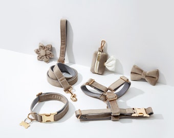 Puede incluir: Un conjunto de accesorios para perros de color marrón claro, que incluye un collar, una correa, un arnés, una pajarita y un porta bolsas para excrementos. Los accesorios están hechos de terciopelo y tienen detalles dorados.
