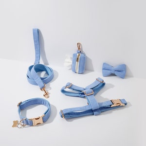 Op de afbeelding: Een set lichtblauwe hondenaccessoires, waaronder een riem, een halsband, een harnas, een poepzakhouder en een strik. Alle items zijn gemaakt van een zachte, corduroy-achtige stof.