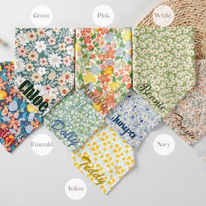 May include: A collection of colorful floral patterned dog bandanas in various colors, including blue, green, pink, and yellow. Each bandana is personalized with a name in a complementary color. The bandanas are arranged on a neutral background.