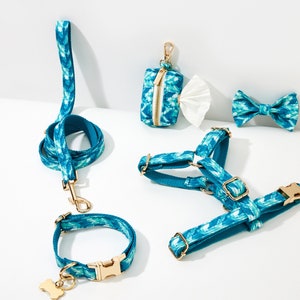 Op de afbeelding: Een tealblauwe hondenharnas, riem, halsband en strik met een gouden gesp en een tealblauw en wit patroon. Een tealblauwe en witte tas met een gouden rits is ook inbegrepen.