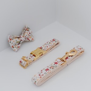 May include: A floral patterned dog collar and leash set with a gold buckle and clasp. The collar has the word "Luxe" engraved on the buckle.