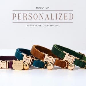 May include: Three personalised leather dog collars with gold-tone hardware and engraved names. The collars are in green, brown, and purple.