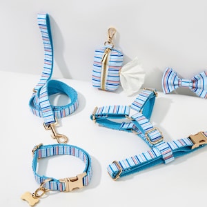 May include: A collection of dog accessories in a blue and white striped pattern. The set includes a leash, collar, harness, bow tie, and waste bag dispenser. All pieces have gold-colored hardware.