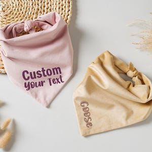 Puede incluir: Dos pa&ntilde;uelos para mascotas. Uno es rosa claro con el texto "Custom your Text" en morado oscuro. El otro es de color canela con el texto "Goose" en marr&oacute;n. Ambos pa&ntilde;uelos est&aacute;n anudados en la parte superior.