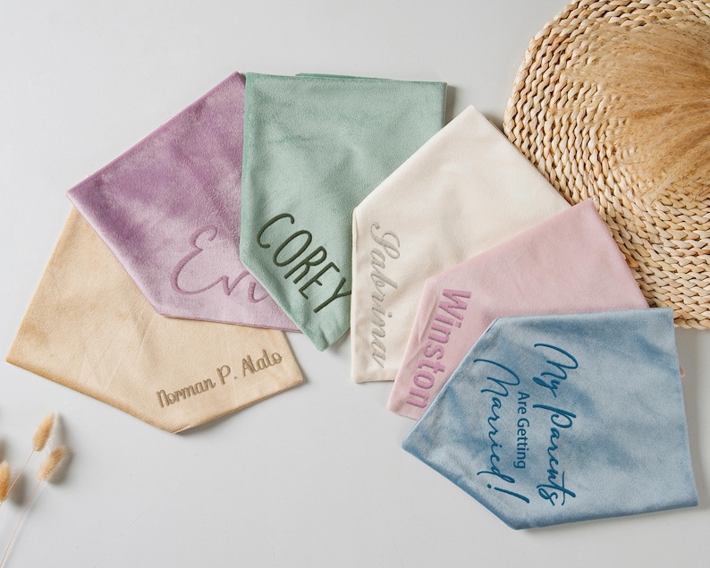 Puede incluir: Una colecci&oacute;n de pa&ntilde;uelos de tela suave personalizados en varios colores pastel, incluyendo lavanda, verde salvia y rosa p&aacute;lido. Cada pa&ntilde;uelo presenta texto bordado, con nombres y frases como "My Parents Are Getting Married!"
