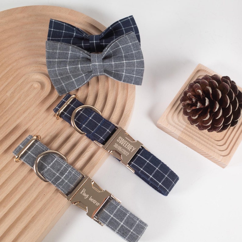 Puede incluir: Dos collares para perros con etiquetas de nombre grabadas personalizadas. Un collar es azul marino con estampado a cuadros blancos y dice "SWEENY 30/09/2022". El otro collar es gris con estampado a cuadros blancos y dice "Pug Beaver".