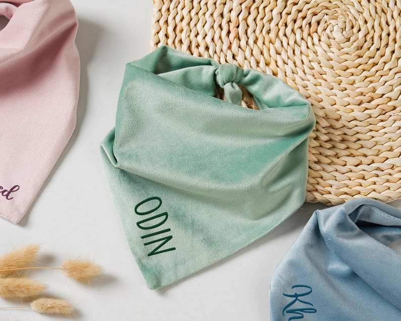 Puede incluir: Primer plano de tres pa&ntilde;uelos de terciopelo en colores pastel: rosa, verde menta y azul. El pa&ntilde;uelo verde menta tiene bordado el nombre "ODIN". Los pa&ntilde;uelos se muestran sobre una superficie blanca con una cesta tejida en el fondo.
