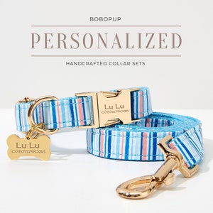 May include: Personalized dog collar and leash set with blue, white, and coral stripes. The gold-colored buckle and tag are engraved with the name "Lu Lu" and a phone number. The text "BOBOPUP" and "PERSONALIZED HANDCRAFTED COLLAR SETS" are displayed.