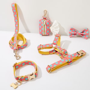 May include: A pink and blue polka dot dog harness, leash, collar, and bow tie. A matching pink and blue polka dot poop bag dispenser is also included.