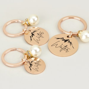 May include: Three rose gold keychains with a mountain silhouette and the name "Walter" engraved on each. Each keychain has a pearl charm.