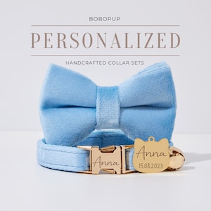 Op de afbeelding: Een lichtblauwe fluwelen kattenhalsbandset met een bijpassende strik. De halsband heeft een gouden gesp met de naam "Anna" erop gegraveerd. Het label heeft ook de datum "15.08.2023" erop gegraveerd.