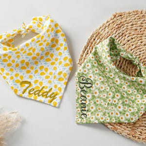 May include: Two pet bandanas. One is white with yellow lemon and blue leaf pattern, the name "Teddy" is embroidered in gold. The other is green with white daisy pattern, the name "Beanie" is embroidered in black.