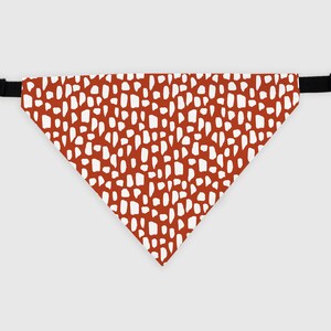 May include: A red and white patterned dog bandana with black adjustable straps. The bandana has a white abstract pattern on a red background.