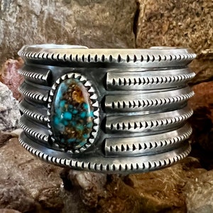 Könnte beinhalten: Ein silbernes Armreif mit einem Türkis-Stein in der Mitte. Das Armband hat ein strukturiertes Design mit mehreren Bändern.