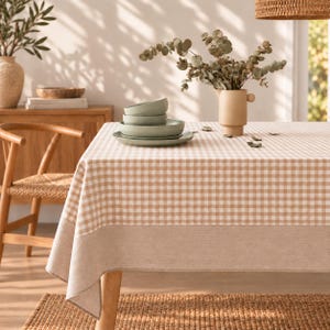 May include: A rectangular tablecloth featuring a beige and white gingham check pattern with a solid beige border along the edges. The fabric drapes over a table, providing a neutral foundation for the dining setting displayed on the surface.