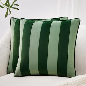 May include: Two green striped throw pillows with dark green piping. The pillows have alternating vertical stripes of light and dark green. The pillows are placed on a white sofa. Decorative pillows for home decor.