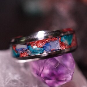 May include: A silver ring with a band of blue, white, and red stones set in a silver band.