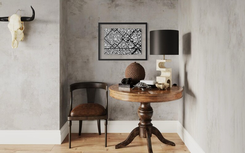 May include: A round wooden pedestal table with a dark brown finish, a dark wood chair with a brown seat, a black-framed abstract art print, a black lamp with a sculptural base, a brown textured sphere, and a white animal skull wall mount.