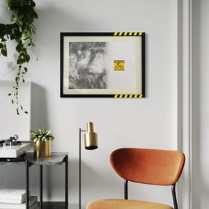 May include: A rectangular framed print featuring a split design with a black and white nebula on the left and a white background on the right. A yellow and black caution sign with the text CAUTION AREA UNDER CONSTRUCTION is centered.
