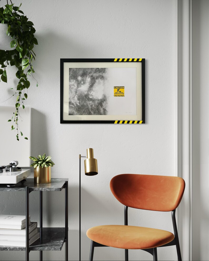 May include: A rectangular framed print featuring a split design with a black and white nebula on the left and a white background on the right. A yellow and black caution sign with the text CAUTION AREA UNDER CONSTRUCTION is centered.