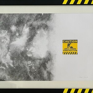 May include: A framed print featuring a black and white stippled nebula on the left transitioning to a white background on the right. A yellow and black caution sign with the text CAUTION AREA UNDER CONSTRUCTION is centered on the right side.