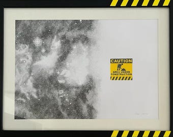 May include: A framed print featuring a black and white stippled nebula on the left transitioning to a white background on the right. A yellow and black caution sign with the text CAUTION AREA UNDER CONSTRUCTION is centred on the right side.