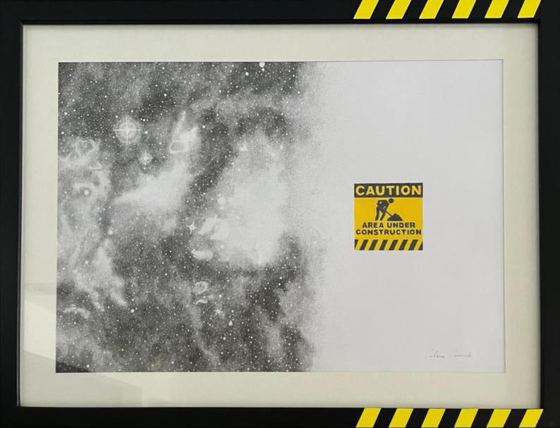 May include: A framed print featuring a black and white stippled nebula on the left transitioning to a white background on the right. A yellow and black caution sign with the text CAUTION AREA UNDER CONSTRUCTION is centered on the right side.