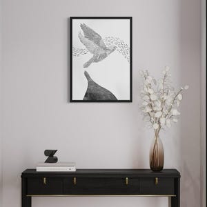 K&ouml;nnte beinhalten: Ein schwarz gerahmter Kunstdruck mit einer detaillierten schwarz-wei&szlig;en Illustration eines fliegenden Vogels &uuml;ber einem dunklen Berggipfel, platziert &uuml;ber einem schwarzen Konsolentisch mit goldenen Beschl&auml;gen, einer Glasvase und B&uuml;chern.