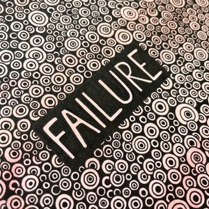 May include: Black and white background with a pattern of concentric circles in shades of pink. The word "FAILURE" is written in white letters on a black rectangle.