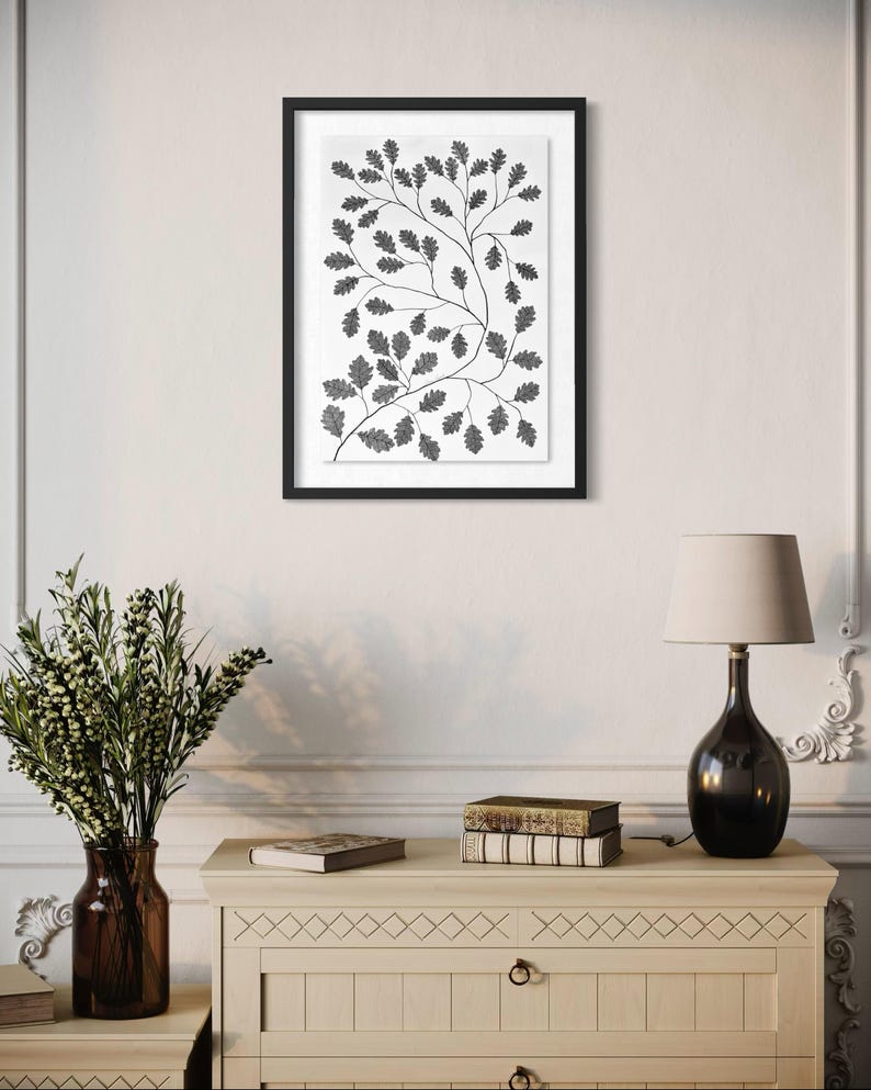 Pu&ograve; includere: Una stampa artistica da parete incorniciata che presenta un'illustrazione botanica in bianco e nero di rami di quercia con foglie dettagliate. L'opera &egrave; presentata in una sottile cornice nera con un passe-partout bianco, mostrando un motivo di fogliame.