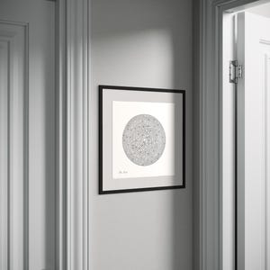 May include: A square black frame containing a white print with a circular maze design in black ink. The artwork features a central labyrinth pattern with a small signature in the bottom left corner, displayed on a light grey wall between two white doors.