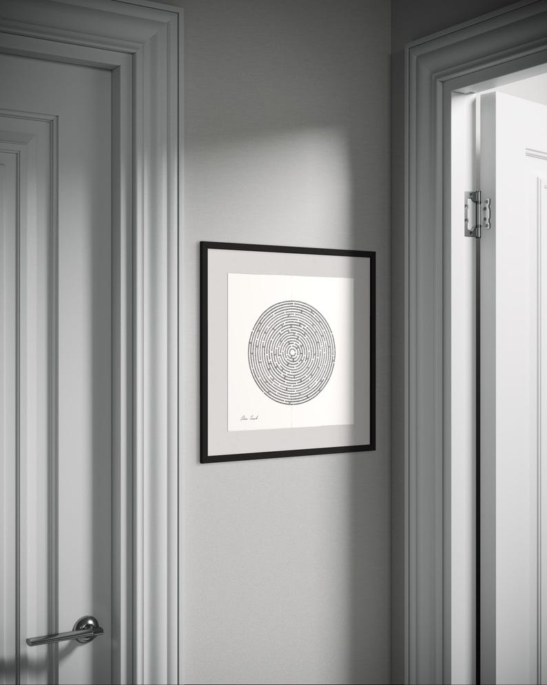 May include: A square black frame containing a white print with a circular maze design in black ink. The artwork features a central labyrinth pattern with a small signature in the bottom left corner, displayed on a light grey wall between two white doors.