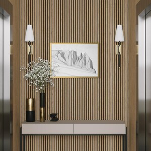 May include: A console table with a light grey top and black legs sits against a vertical wood slat wall. Two wall sconces with white shades flank a framed black and white mountain sketch. Two cylindrical vases hold white flowers.
