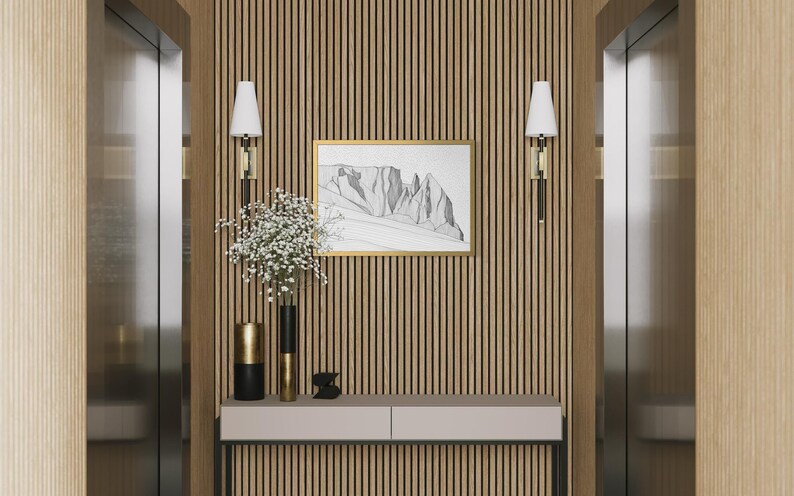 May include: A console table with a light grey top and black legs sits against a vertical wood slat wall. Two wall sconces with white shades flank a framed black and white mountain sketch. Two cylindrical vases hold white flowers.