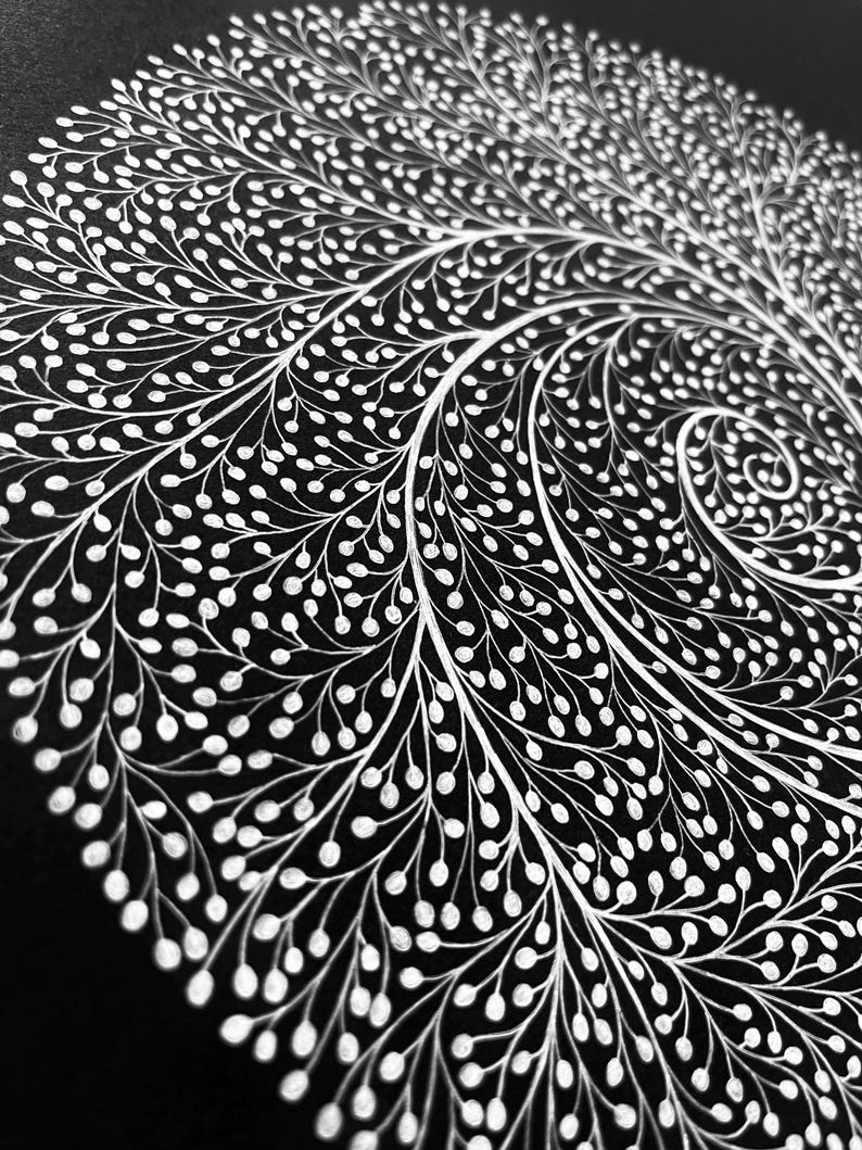 May include: A circular artwork featuring a dense, white ink illustration on a solid black background. The design consists of intricate, branching lines that spiral outward from the center, ending in small, rounded white dots resembling seeds.