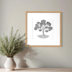 May include: A square framed wall art piece featuring a black and white ink illustration of a tree with a detailed root system and a full canopy of leaves, enclosed in a light-toned wooden frame with a white mat border.