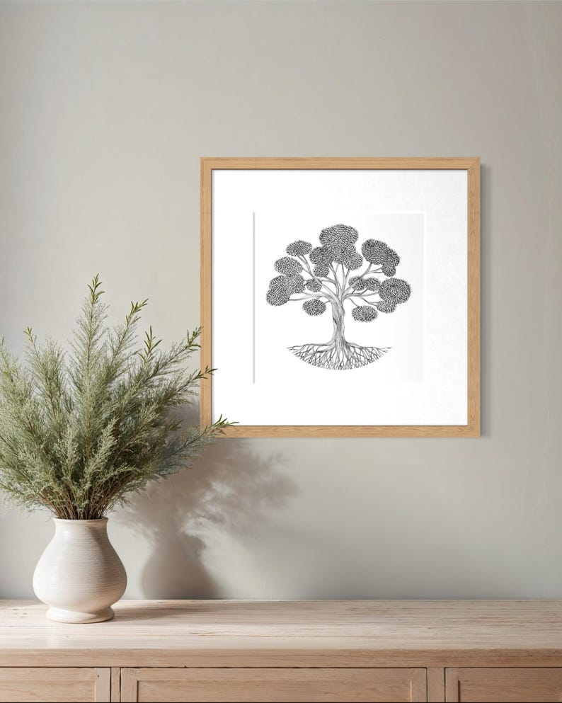 May include: A square framed wall art piece featuring a black and white ink illustration of a tree with a detailed root system and a full canopy of leaves, enclosed in a light-toned wooden frame with a white mat border.