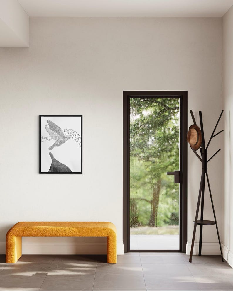 K&ouml;nnte beinhalten: Ein rechteckiger, schwarz gerahmter Kunstdruck mit einer monochromen Illustration eines fliegenden Vogels &uuml;ber einer dunklen Form, platziert &uuml;ber einer senfgelben Polsterbank neben einem dunkelbraunen Garderobenst&auml;nder mit Hut.